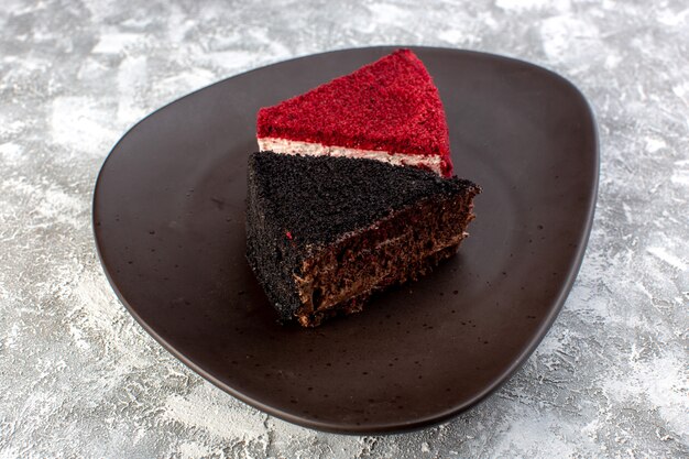 Vue rapprochée avant de tranches de gâteau de couleur chocolat et morceaux de gâteau aux fruits à l'intérieur de la plaque brune sur la surface grise