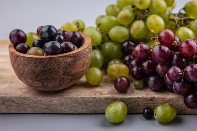 Vue rapprochée de baies de raisin dans un bol et de raisins sur une planche à découper sur fond gris