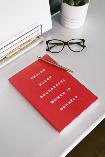 Vue rapprochée d'un bureau blanc avec cahier rouge, stylo et lunettes en c