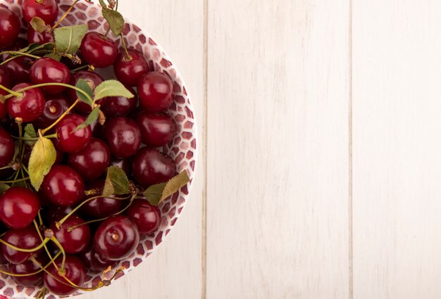 Vue rapprochée de cerises avec des feuilles dans un bol sur fond de bois avec espace copie