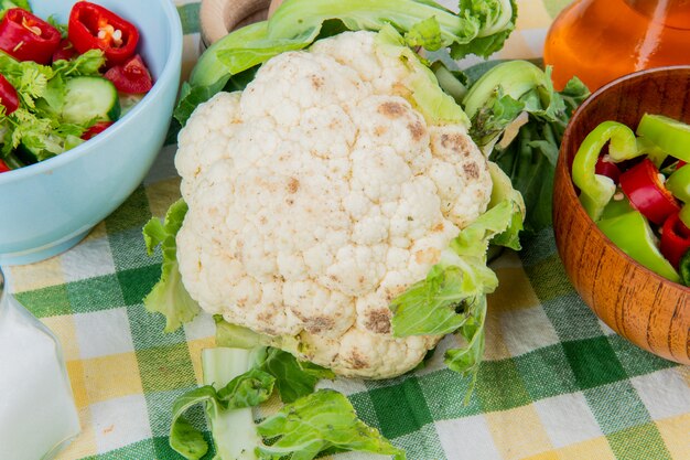 Vue rapprochée de chou-fleur avec des poivrons en tranches et une salade de légumes avec du beurre fondu et du sel sur un tissu écossais