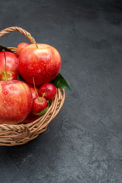 Vue rapprochée de côté fruits les cerises et pommes appétissantes avec des feuilles dans le panier