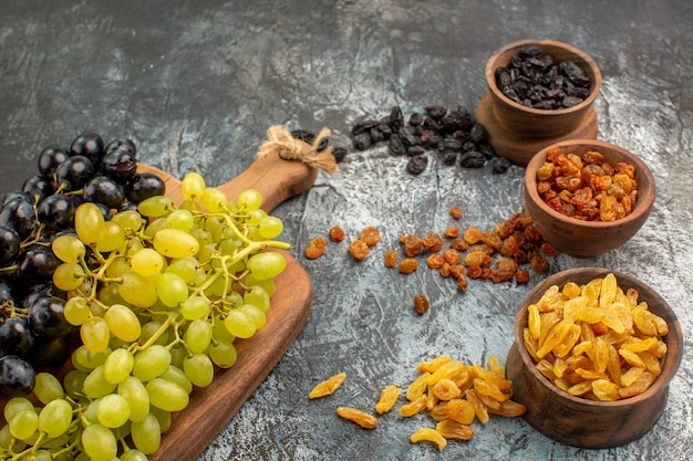 Photo gratuite vue rapprochée de côté fruits secs fruits secs dans les bols bruns et raisins sur la planche de bois