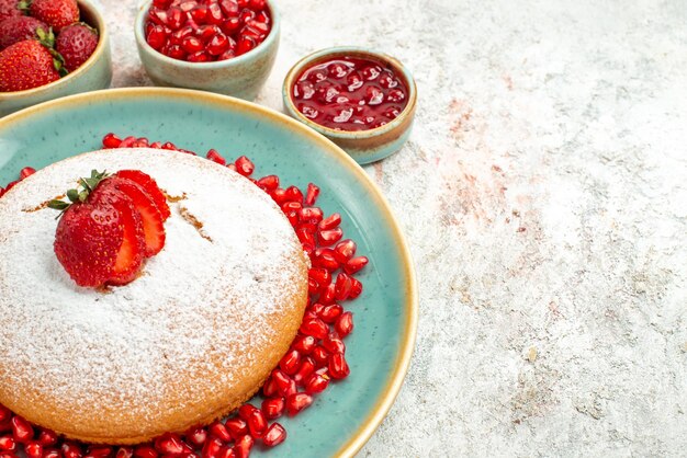 Vue rapprochée de côté gâteau appétissant gâteau de fraises et de grenade et les bols de baies sur la table