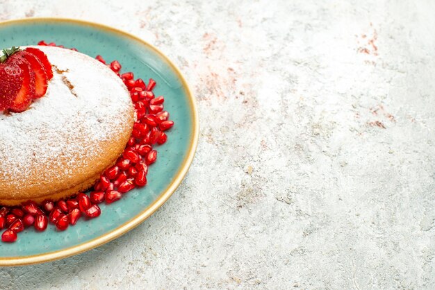 Vue rapprochée de côté gâteau appétissant à la grenade et aux fraises avec des fraises et de la grenade sur la table rose-gris