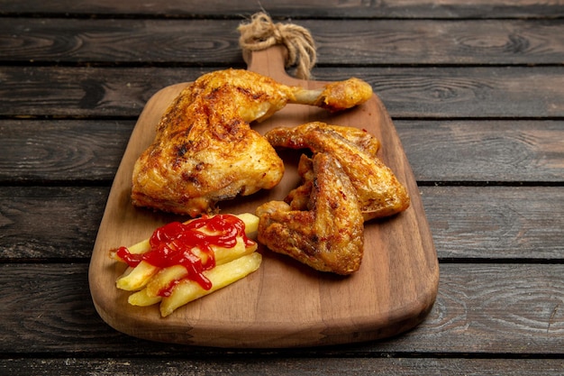 Vue rapprochée de côté poulet et épices ailes et cuisse de poulet avec frites et ketchup sur la planche à découper au centre de la table sombre