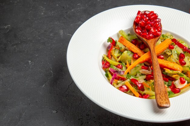 Vue rapprochée de côté salade de légumes grenade et cuillère avec des graines de grenades