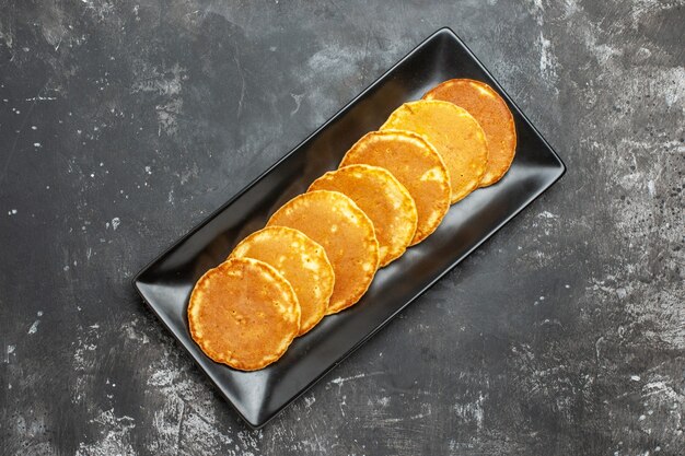 Vue rapprochée de crêpes maison alignées sur une plaque noire de forme carrée sur fond gris