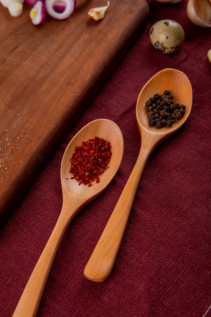 Photo gratuite vue rapprochée de cuillères en bois avec des épices comme du sumac et des grains de poivre noir sur fond bordeaux