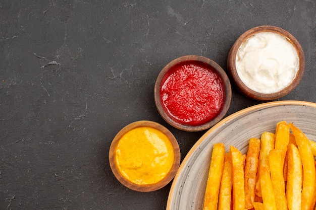 Photo gratuite vue rapprochée de délicieuses frites avec des assaisonnements sur un espace sombre