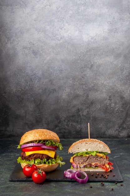 Vue rapprochée de délicieux sandwichs entiers coupés et de tomates avec des oignons de tige sur un plateau noir sur une surface de couleur sombre