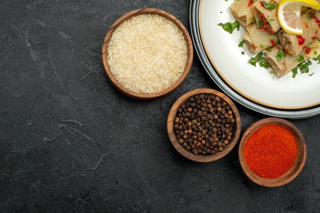 Vue rapprochée de dessus assiette blanche de chou farci aux herbes citron et sauce sur assiette blanche et bols d'épices colorées poivre noir et riz sur la table