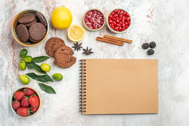 Vue rapprochée de dessus biscuits au chocolat crème cahier biscuits au chocolat bols de baies agrumes bâtons de cannelle sur la table