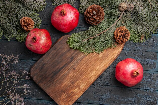 Vue Rapprochée De Dessus Branches Et Grenades Grenades Rouges Appétissantes à Côté De La Planche à Découper Deux Grenades Et Branches Avec Des Cônes Sur Une Surface Grise