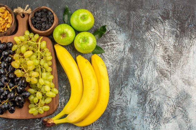 Vue rapprochée de dessus fruits bananes bols de fruits secs pommes avec feuilles et raisins sur le plateau