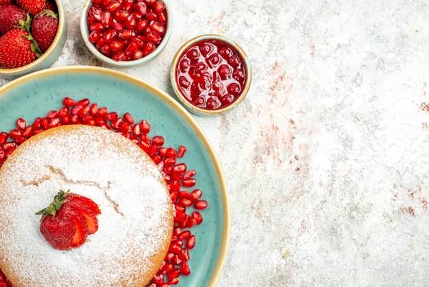 Vue rapprochée de dessus un gâteau appétissant à la grenade et aux fraises à côté des bols de fraises et de grenade sur la table