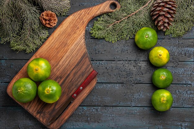 Vue rapprochée de dessus limes et branches trois limes vert-jaune et couteau sur la planche à découper à côté des limes et des branches d'arbres et des cônes