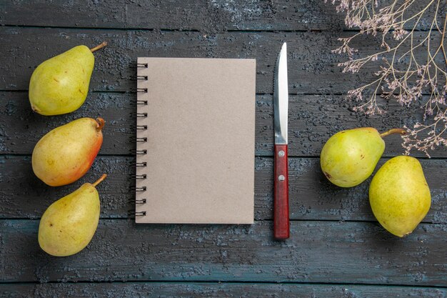 Vue rapprochée de dessus poires et cahier gris cahier et couteau entre des poires appétissantes à côté de branches d'arbres