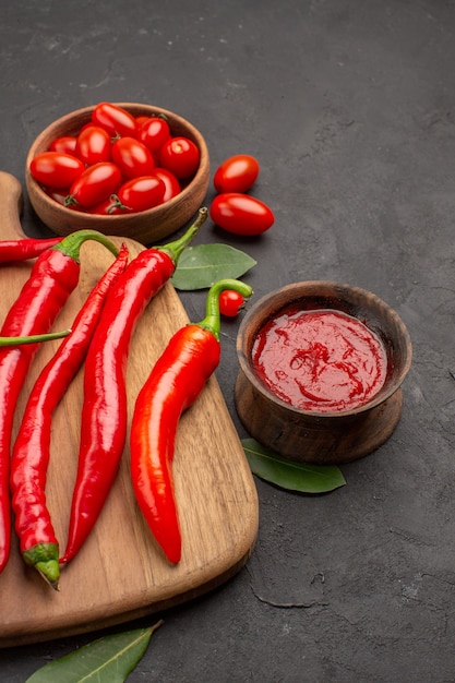 Vue rapprochée du bas un bol de tomates cerises piments rouges chauds sur la planche à découper les feuilles de laurier et un bol de ketchup sur la table noire