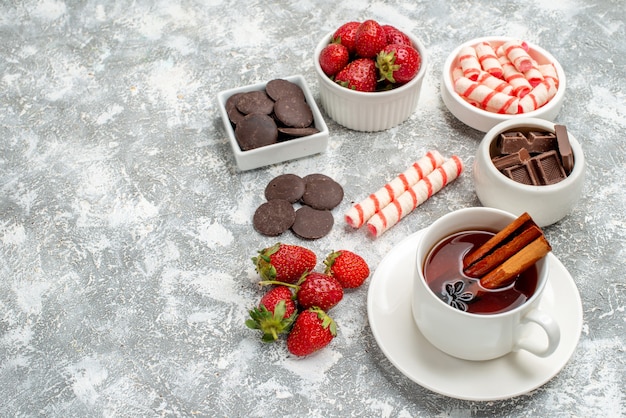 Vue rapprochée du bas bols avec bonbons chocolats fraises et thé aux graines d'anis cannelle sur le côté droit de l'arrière-plan gris-blanc