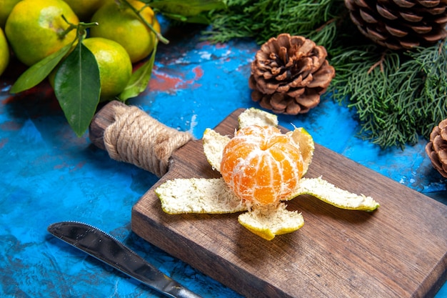 Vue Rapprochée Du Bas Mandarine Pelée Un Couteau De Table Sur Une Planche à Découper Des Mandarines Fraîches Avec Des Feuilles De Branches De Pin Sur Fond Bleu