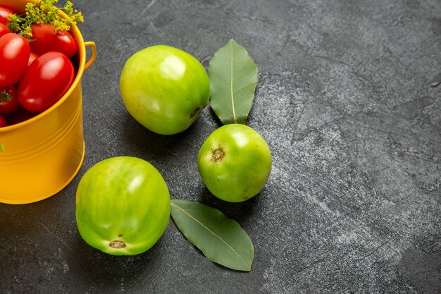 Vue rapprochée du bas seau jaune rempli de tomates cerises et de fleurs d'aneth feuilles de laurier et tomates vertes sur fond sombre