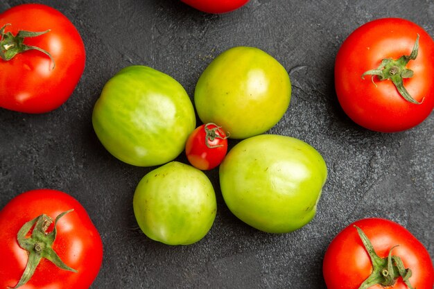 Vue rapprochée du bas des tomates rouges et vertes autour d'une tomate cerise sur table sombre