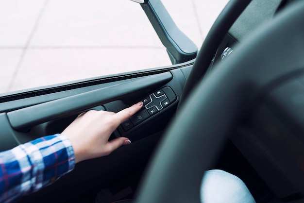 Vue rapprochée du contrôle du véhicule Windows et des mains du conducteur en appuyant sur le bouton pour enrouler la fenêtre dans le véhicule