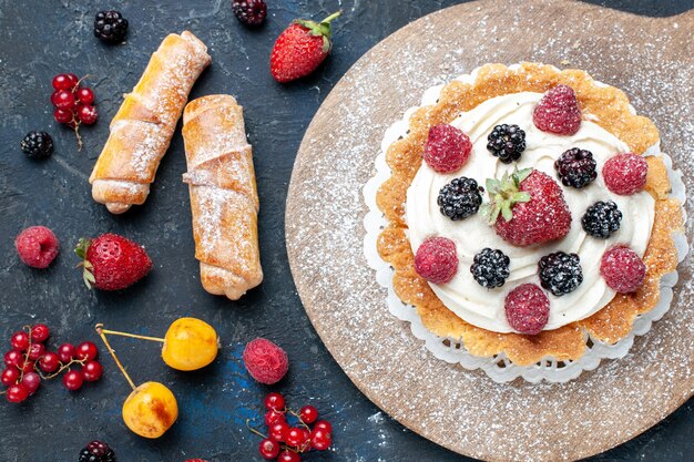 Vue rapprochée du délicieux petit gâteau avec de la crème de sucre en poudre et des baies avec des bracelets sur un bureau sombre