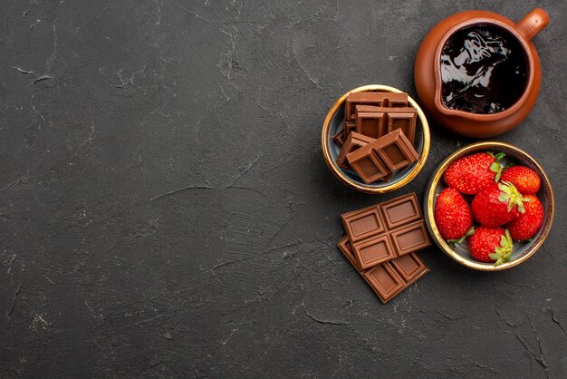 Vue rapprochée du dessus chocolat sur table fraises dans une assiette bol de crème au chocolat et barres de chocolat sur le côté droit de la table