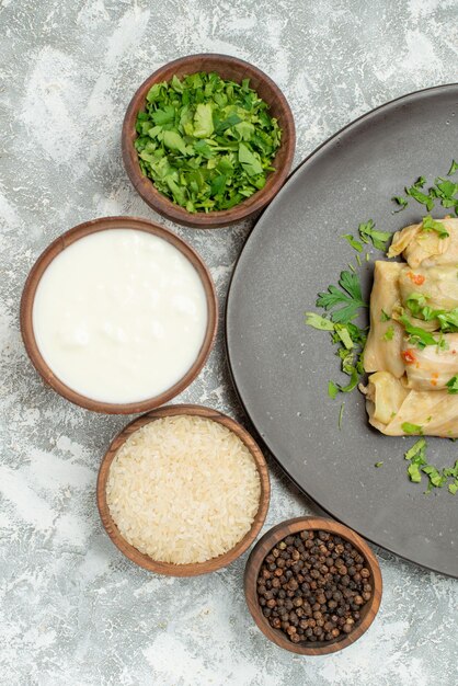 Vue rapprochée du haut de l'assiette de chou farci bols de riz à la crème sure aux herbes et poivre noir à côté d'une assiette grise de chou farci sur la table