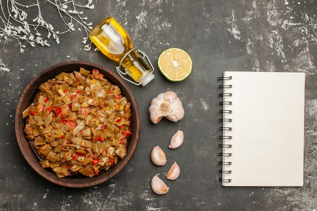 Vue rapprochée du haut assiette de haricots verts bouteille d'huile ail citron cahier blanc à côté de l'assiette de haricots verts avec tomates sur le tableau noir