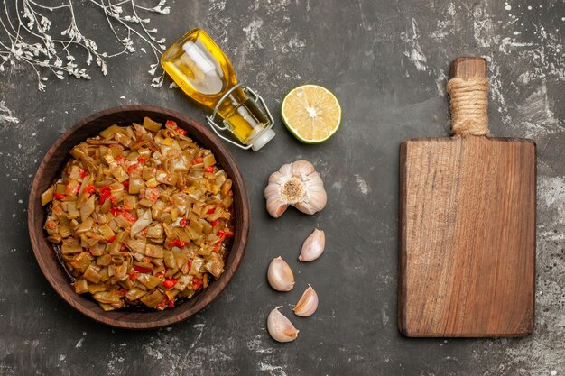 Photo gratuite vue rapprochée du haut de l'assiette de haricots verts bouteille d'huile d'ail citron à côté de l'assiette de haricots verts et de tomates et de la planche à découper en bois sur le tableau noir