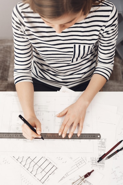 Vue rapprochée du haut de la belle jeune femme architecte concentré faisant son nouveau projet d'appartements, à l'aide d'une règle et d'un stylo