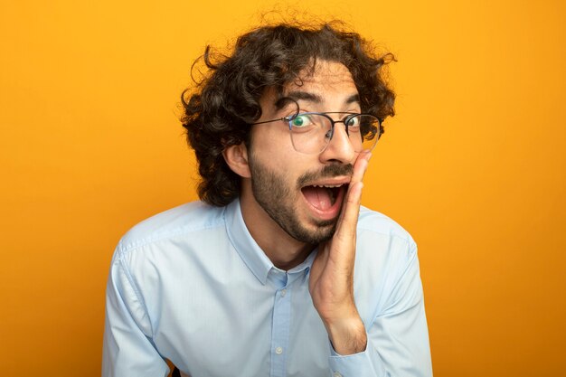 Vue rapprochée du jeune bel homme caucasien portant des lunettes isolé sur mur orange