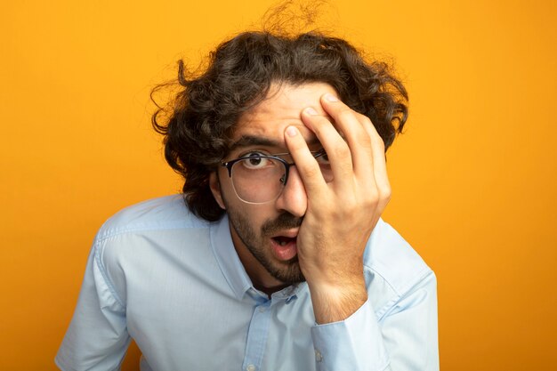 Vue rapprochée du jeune bel homme portant des lunettes regardant avant isolé sur mur orange