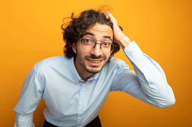 Vue rapprochée du jeune bel homme portant des lunettes regardant avant isolé sur mur orange