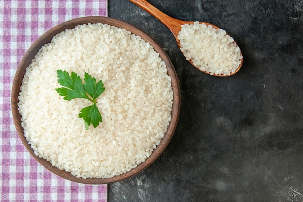 Vue rapprochée du riz rond parfait dans un bol marron avec du vert sur une serviette dépouillée violette et dans une cuillère en bois sur fond de couleur foncée