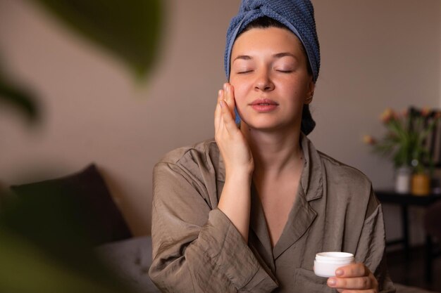 Vue rapprochée d'une femme fraîche avec de la crème sur le visage à la maison en regardant un miroir