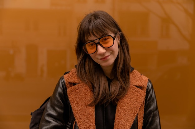 Vue rapprochée d'une femme souriante dans des lunettes de soleil orange près du mur en regardant la caméra