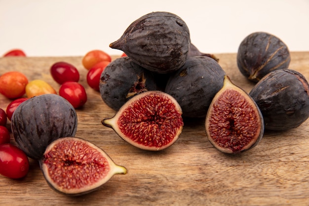 Photo gratuite vue rapprochée de figues noires sucrées sur une planche de cuisine en bois avec des cerises cornaline isolé sur un mur blanc