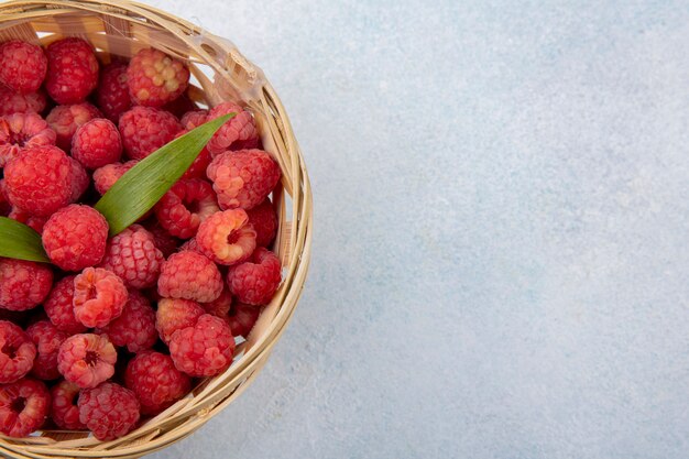 Vue rapprochée de framboises avec des feuilles dans le panier sur une surface blanche