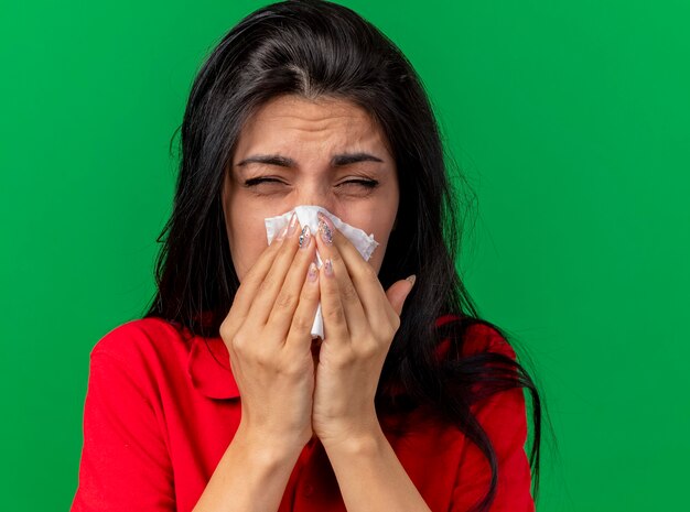 Vue rapprochée de froncer les sourcils jeune femme malade essuyant le nez avec serviette avec les yeux fermés isolé sur mur vert