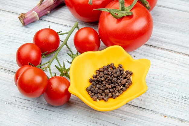 Vue rapprochée des graines de poivre noir dans un bol et des tomates sur une table en bois