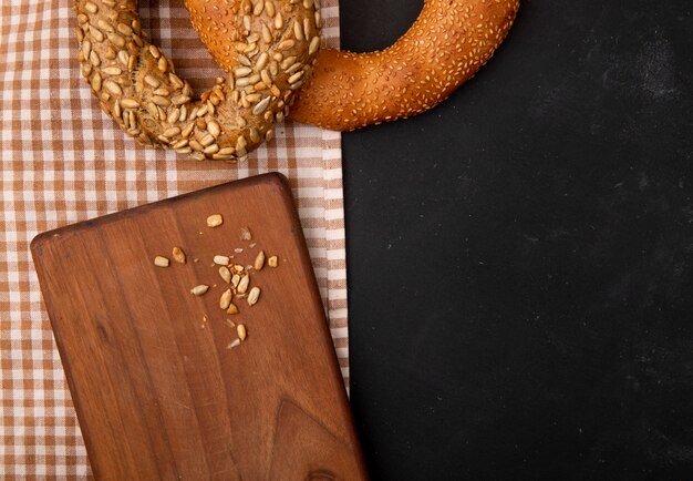 Vue rapprochée de graines de tournesol sur planche à découper et bagels sur tissu sur fond noir avec copie espace