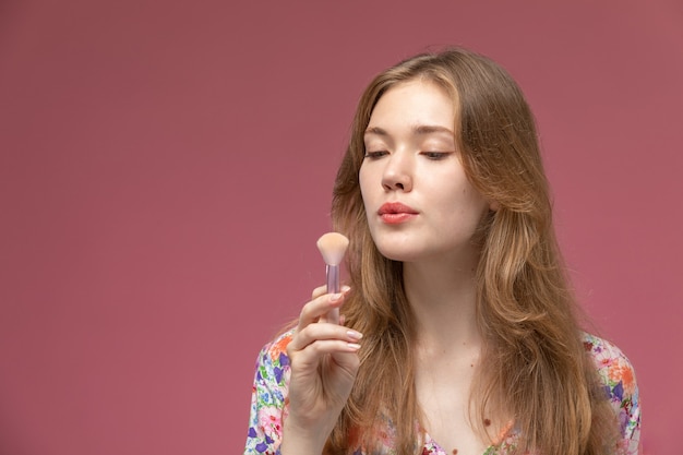 Vue rapprochée jolie femme nettoyant son pinceau à poudre sur mur rouge