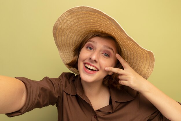 Vue rapprochée de joyeuse jeune fille blonde faisant signe de paix tendant la main vers la caméra