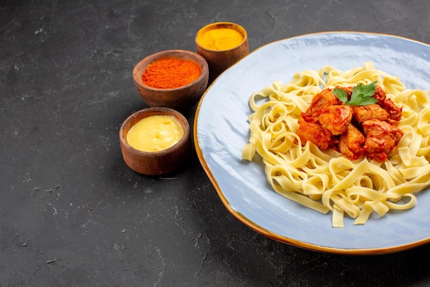 Vue rapprochée latérale de l'assiette de pâtes pâtes appétissantes avec sauce et viande à côté des bols de sauces colorées sur la table sombre