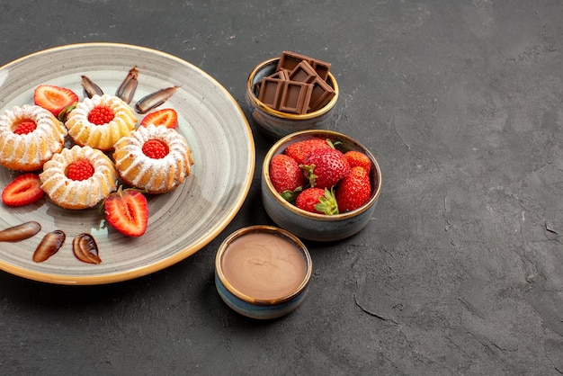 Vue rapprochée latérale biscuits aux fraises au chocolat bols gris de fraises chocolat et crème au chocolat à côté de l'assiette de biscuits aux fraises sur la table