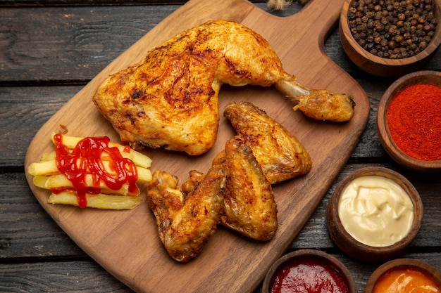 Vue rapprochée latérale des bols de poulet et d'épices de sauces et d'épices et de poulet et de frites sur la planche à découper